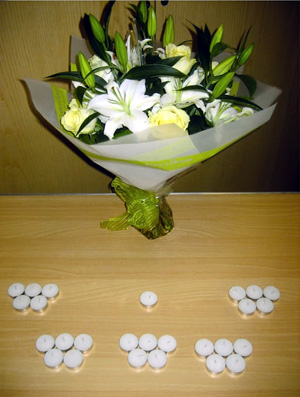 The focal point is a table with a vase of white lilies and roses, and 25 + 1 candles